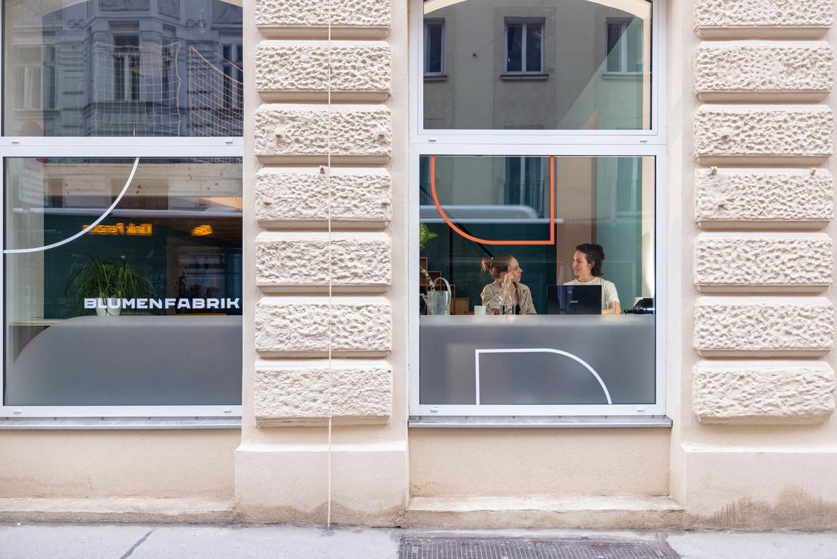 Zwei Frauen sitzen an Fensterbank, arbeiten am Laptop und reden mit einander.