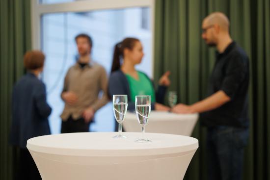 Zwei Sektgläser im Fokus. Im Hintergrund sieht man vier Menschen miteinander reden.