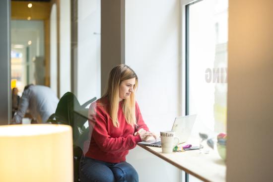 Eine Frau arbeitet am Laptop an einer Fensterbank