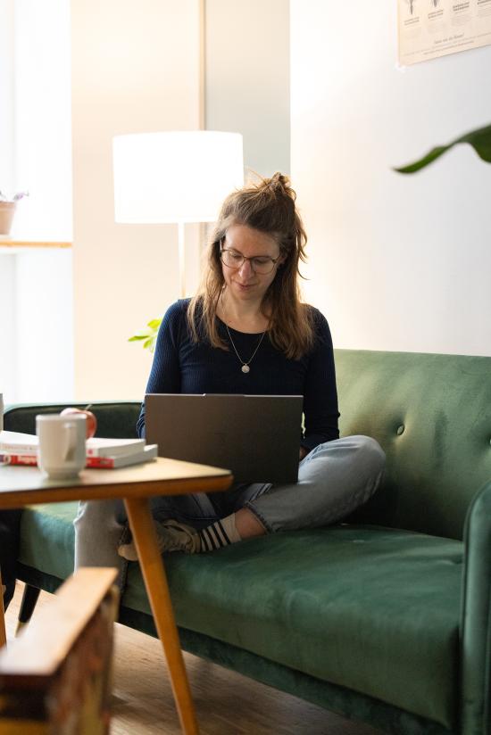 Eine Frau arbeitet am Laptop während sie auf dem Sofa sitzt