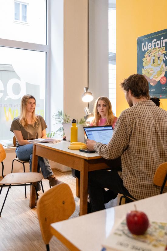 Zwei Frauen und ein Mann arbeiten gemeinsam an einem Tisch. 